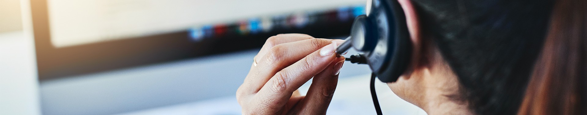 Pessoa de cabelo preso utilizando headset e computador, trabalhando em atendimento ou suporte.